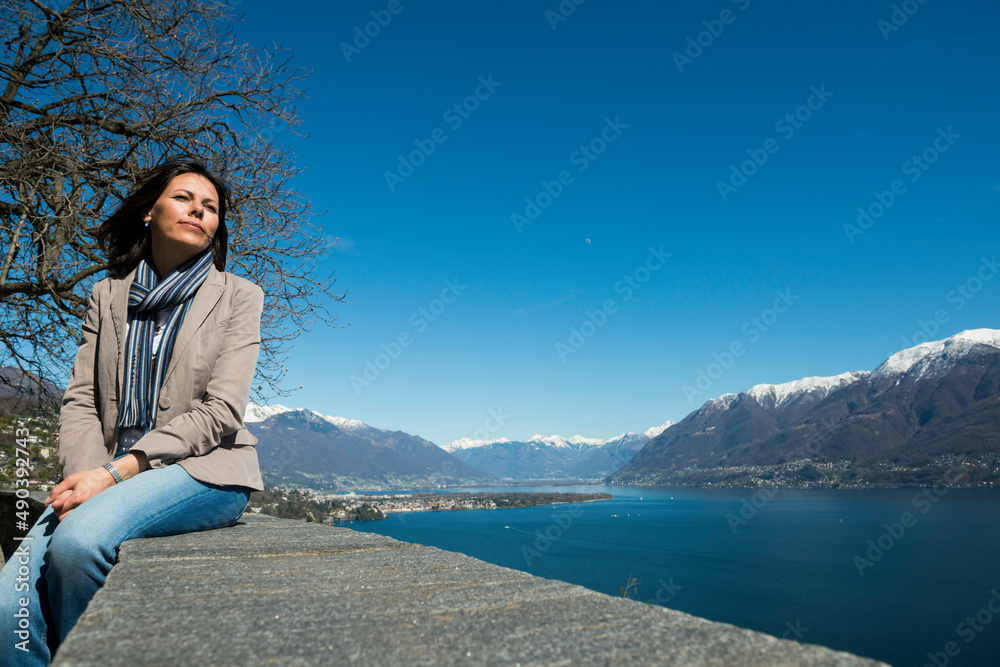 Woman Sitting and Enjoy the Panoramic View over Alpine Lake Maggiore with Snow-capped Mountain in Ascona, Switzerland. Woman Sitting and Enjoy the Panoramic View over Alpine Lake Maggiore with Snow-capped Mountain in Ascona, Switzerland.