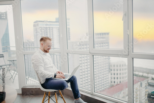 male freelancer works with a laptop in an apartment overlooking the city and the sunset sea.