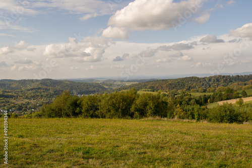 Landscape overlooking high mountains and glades. In the distance a strip of trees and buildings.