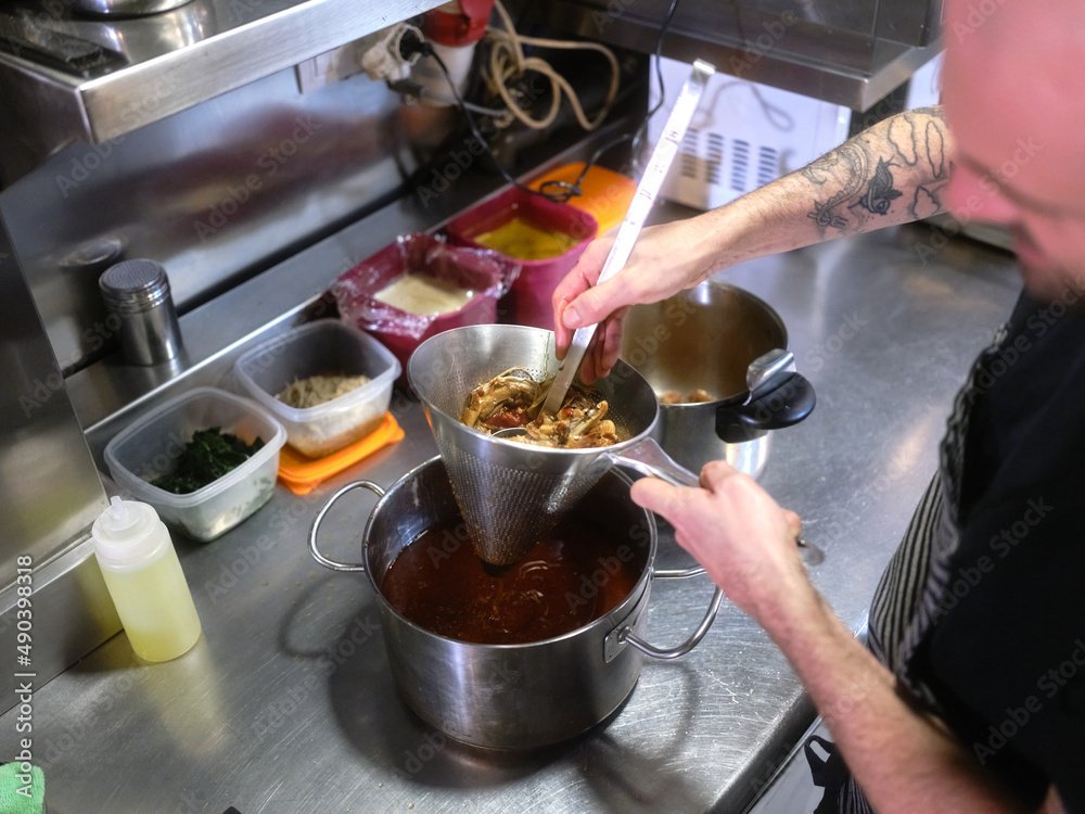 Cook strains food into a pot to prepare a tasting menu in a restaurant