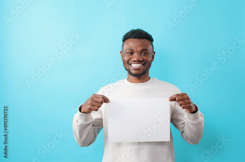 a young smiling African American holds a white sheet in his hands, on a blue isolated background photo