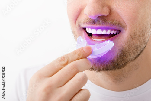 A man holds in his hand an ultraviolet lamp for home teeth whitening. A snow-white smile after bleaching.