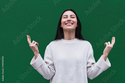Photo Asian woman smiles broadly with eyes closed, keeps fingers crossed, hope for goo