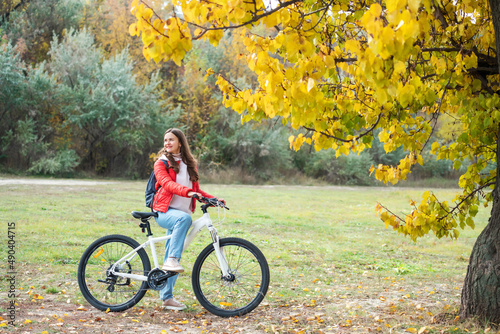 Young woman walk with bicycle and looking at beautiful nature. Female bicyclist enjoying view of autumn or spring outdoors. Concept of sport, biking, active leisure.