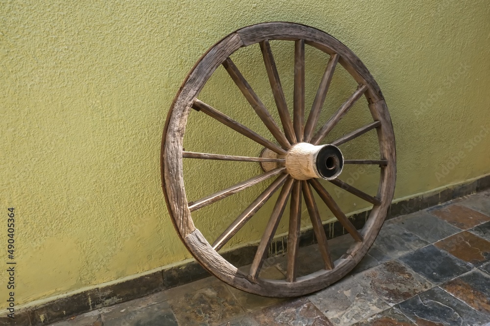 Obsolete vintage wooden wheel on faded yellow wall background