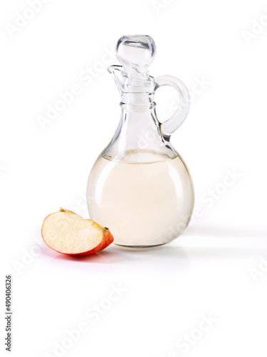 Apple cider vinegar- so many great health benefits. Studio shot of a jug of apple cider vinegar with a slice of apple beside it.