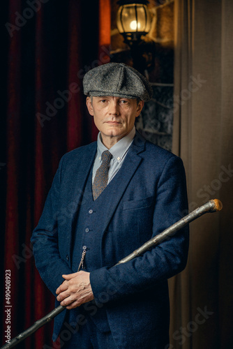 An elderly man in a stylish tweed suit, a flat cap and a cane. Peaky blinders style.
