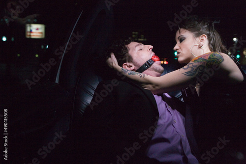 Dominatrix and man wearing ball gag in limousine