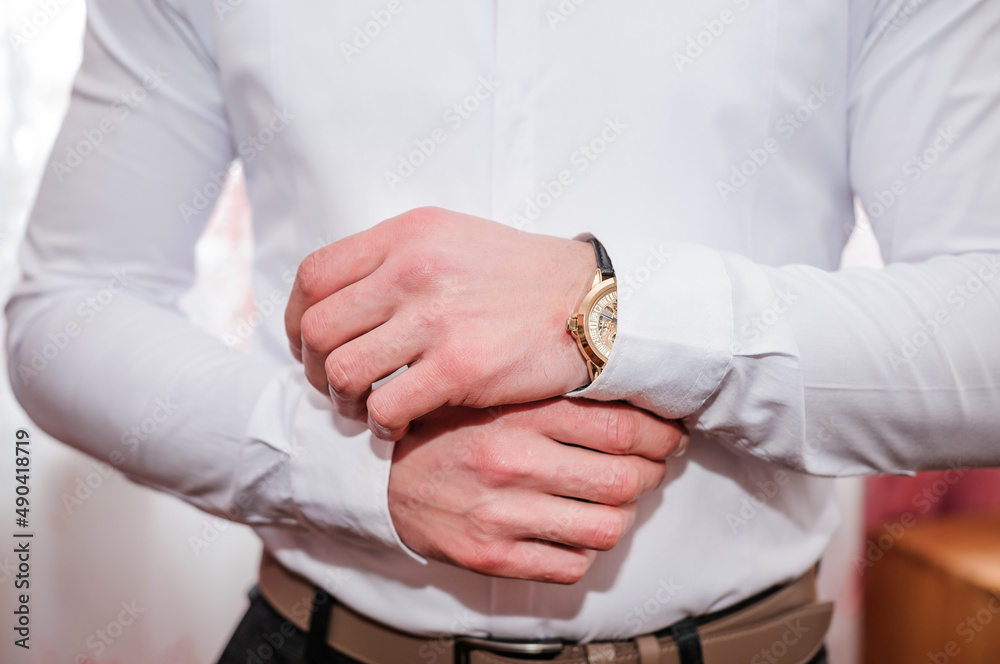 Fototapeta premium A man fastens a cufflink on his shirt. Groom fastening cufflinks on his shirt