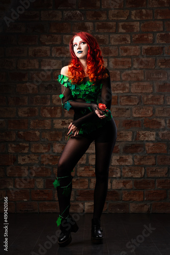 poison ivy comics character cosplay. Halloween costume. young sexy woman in a vine, leaves and poison ivy costume posing as a superhero against brick wall background. female with curly red hair