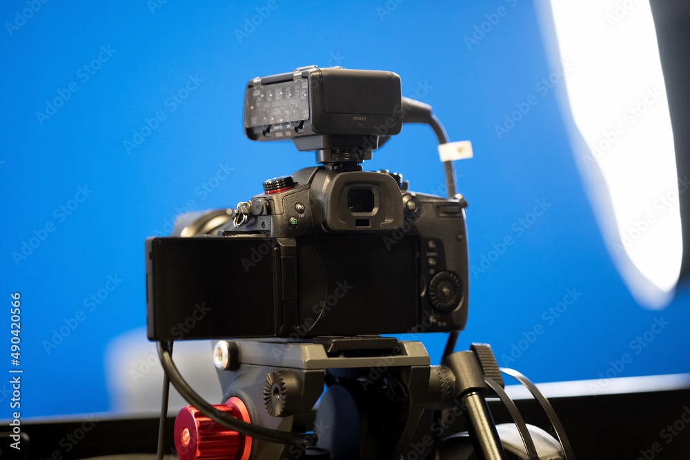 A modern professional high end mirrorless video camera on a tripod stand, bluescreen chroma key studio background, lights, live transmission recording, broadcast, media streaming concept, nobody