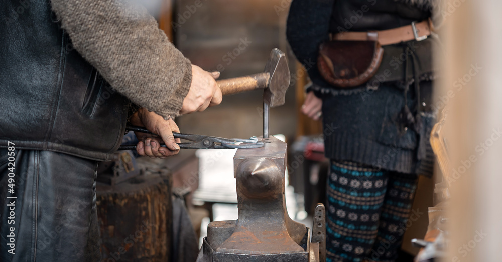 An anonymous smith, blacksmith forging a horseshoe hammering, hitting ...