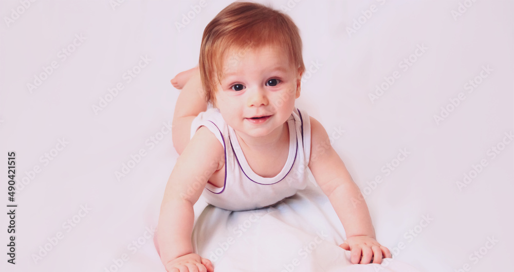 A caucasian baby boy lies in a white bodysuit with a toy on a white background A caucasian baby boy lies in a white bodysuit with a toy on a white background