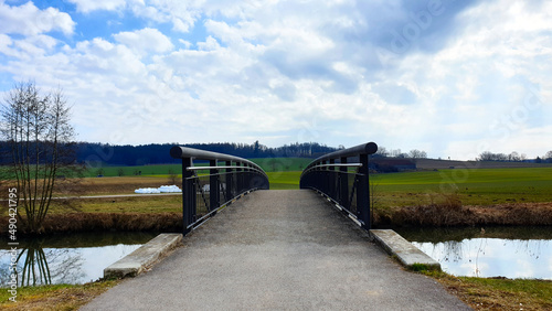 Brücken. Brücke über einen Fluss, der auf eine grüne Wiese und einen blauen Himmel voller Wolken zuführt. Wandern in Bayern Alpen, Deutschland, Europe.