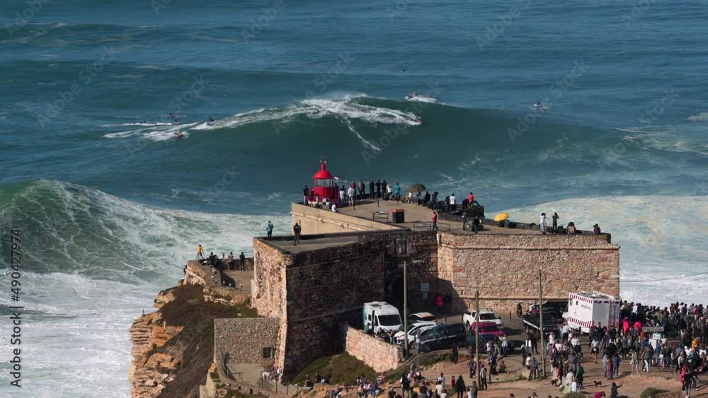 Surfer riding giant wave near historical landmark Fort of Sao Miguel Arcanjo Lighthouse in Nazare, Portugal. Nazare is famously known to surfers for having the largest waves in the world.	
