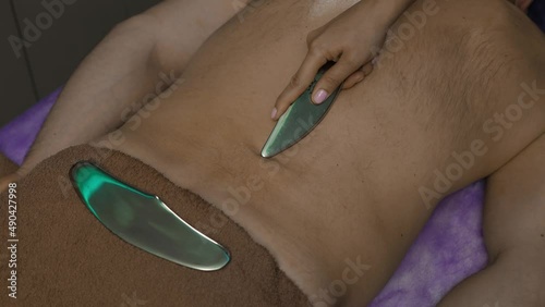 Female hand uses Gua sha scraper tool on male back. Massage with metal object photo