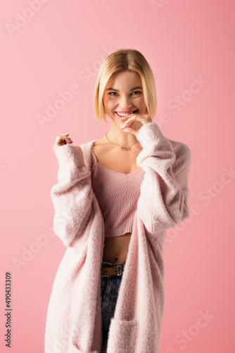 flirty young woman in soft cardigan smiling isolated on pink.