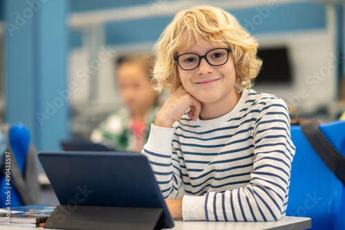 Boy looking at camera sitting at desk with tablet
