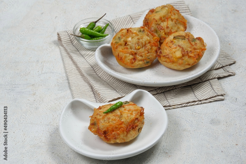 Bakwan Pontianak or vegetable fritters is an Indonesian traditional snack made from wheat flour mixed with vegetables and topping with dried shrimps. Served with sour and spicy sauce in white plate.
