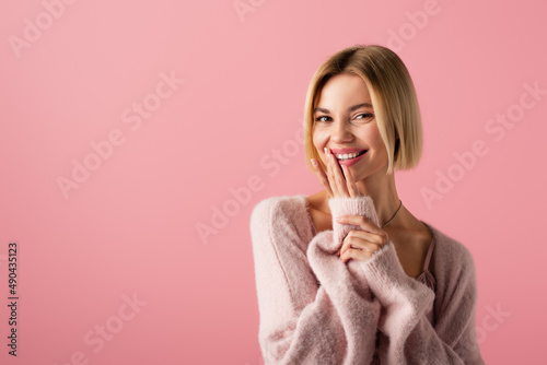 happy young woman in soft cardigan touching lips isolated on pink.