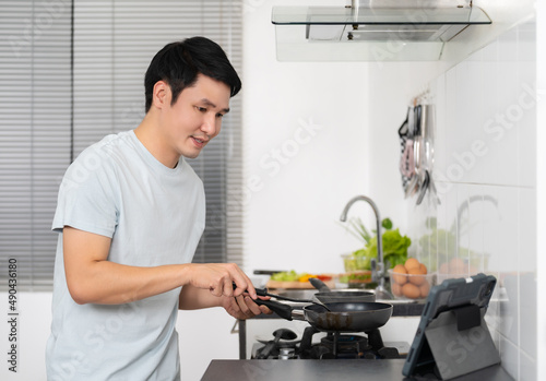 man cooking and preparing food according to a recipe on a tablet computer in the kitchen at home