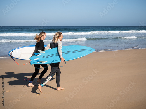 2 surfer women running with surfboards on the beach shore. Happiness, freedom concept.