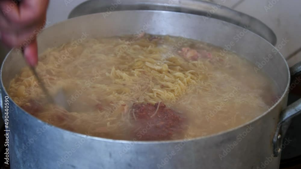 A volunteer cook stirs porridge in a large pot while preparing food for the homeless. A volunteer cook prepares lunch for a group of refugees A volunteer cook stirs porridge in a large pot while preparing food for the homeless. A volunteer cook prepares lunch for a group of refugees