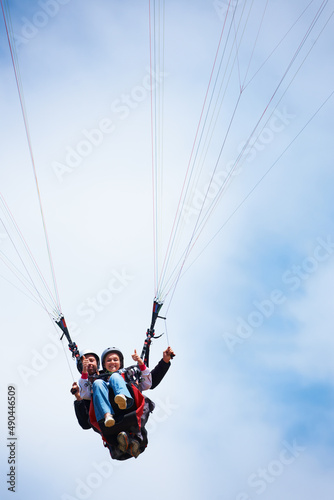 Thumbs up for paragliding. Low angle shot of two people tandem paragliding and giving a thumbs up.