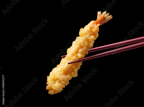 Shrimp tempura lifted with chopsticks against a black background.