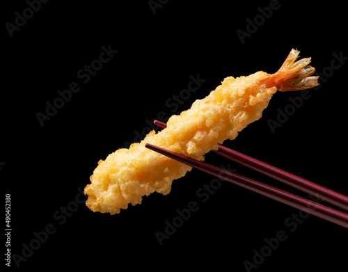 Shrimp tempura lifted with chopsticks against a black background.