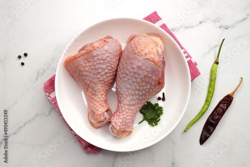 Raw chicken legs or chicken drumsticks with spices on a white plate, Top view with copy space. Biryani cut chicken with skin on. complete animal based Protein source. photo