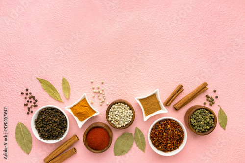 Spices and seasonings in small bowls on pink background, space for text