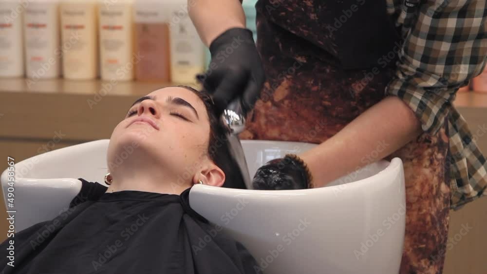 Stylist in gloves and apron rinses root touch up from woman's hair Stylist in gloves and apron rinses root touch up from woman's hair