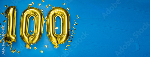 golden yellow foil balloon on blue concrete background number one hundred. Birthday or anniversary card with 100 inscription. Anniversary celebration. photo