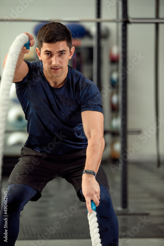 Man sitting on his toes holding a pair of battle ropes for workout. guy at the gym working out with fitness rope. © Georgii