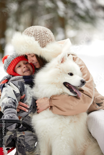 Mother and son child walking with white Samoyed dog in winter day