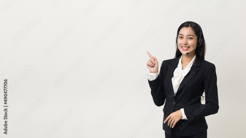 Happy young asian business woman call centre pointing finger to blank space. Welcome female operator put on smalltalk headphone standing on isolated white background. Happy young asian business woman call centre pointing finger to blank space. Welcome female operator put on smalltalk headphone standing on isolated white background.