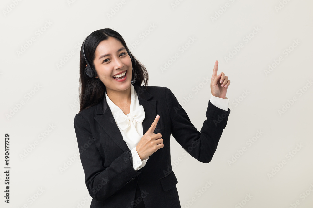 Happy young asian business woman call centre pointing finger to blank space. Welcome female operator put on smalltalk headphone standing on isolated white background. Happy young asian business woman call centre pointing finger to blank space. Welcome female operator put on smalltalk headphone standing on isolated white background.