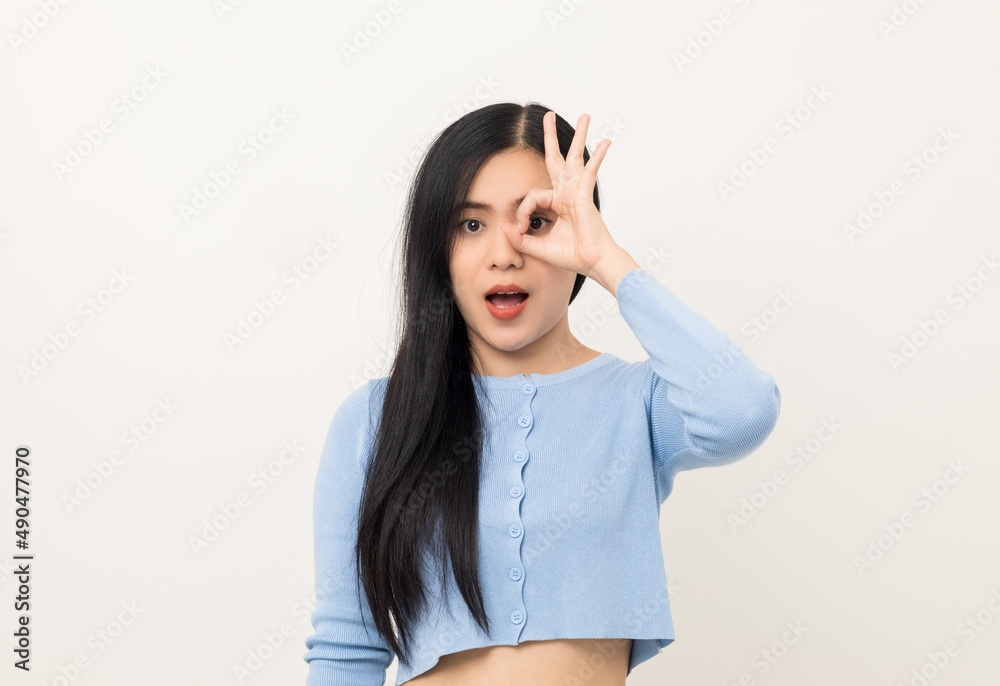 Portrait of Young beautiful Asian woman standing and smiling isolated on white background showing ok sign. Attractive female wearing blue shirt feeling surprised and happy. Portrait of Young beautiful Asian woman standing and smiling isolated on white background showing ok sign. Attractive female wearing blue shirt feeling surprised and happy.