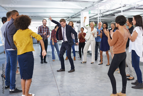 All work and no play.... Shot of a businessman in a suit dancing in the office to cheers from coworkers.