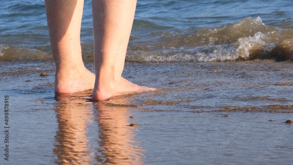 mature female legs are walking along the sandy beach and splashing in the sea on a summer sunny day. Woman walks barefoot on the water close-up mature female legs are walking along the sandy beach and splashing in the sea on a summer sunny day. Woman walks barefoot on the water close-up