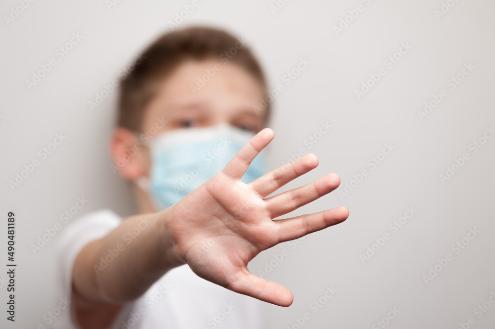 Naklejka premium Caucasian boy in the medical mask and white T-shirt putting his hand forward and stopping something