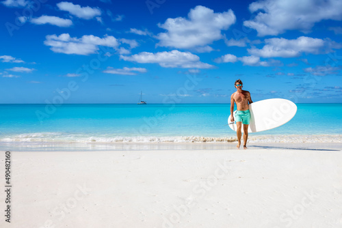 A sportive man in swimshorts with a stand up paddle board walks on a tropical beach