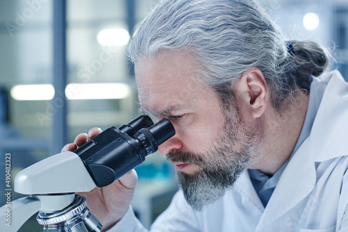 Close-up of bearded doctor examining the virus through the microscope in laboratory