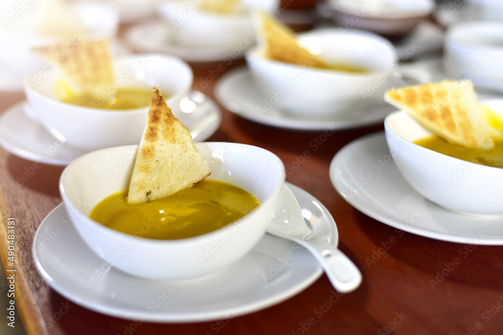 top view of Pumpkin cream soup in a white cup with toast on rustic wooden table. selected focus top view of Pumpkin cream soup in a white cup with toast on rustic wooden table. selected focus