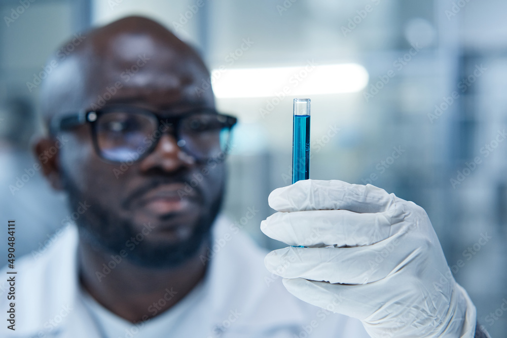 Close-up of African scientist holding flask with sample in protective gloves during medical experiment in laboratory Close-up of African scientist holding flask with sample in protective gloves during medical experiment in laboratory