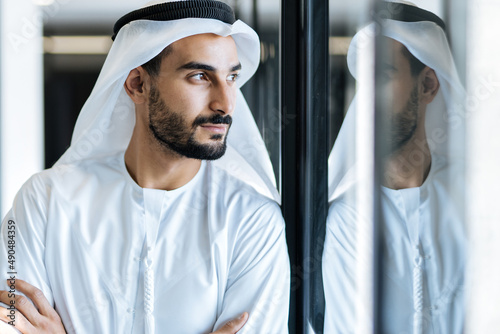 handsome man with dish dasha working in his business office of Dubai. Portraits of a successful businessman in traditional emirates white dress. Concept about middle eastern cultures