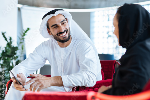 Man and woman with traditional clothes working in a business office of Dubai. Portraits of  successful entrepreneurs businessman and businesswoman in formal emirates outfits.  photo