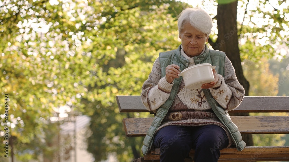 Fototapeta premium Old white-haired homeless woman eating warm meal thanks to the charity volunteers that help people in need. High quality photo