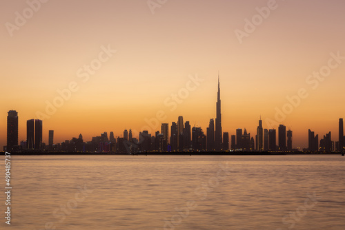 Skyline of Dubai Business Bay with silhouettes of buildings during hazy sunset, orange colors, long exposure.